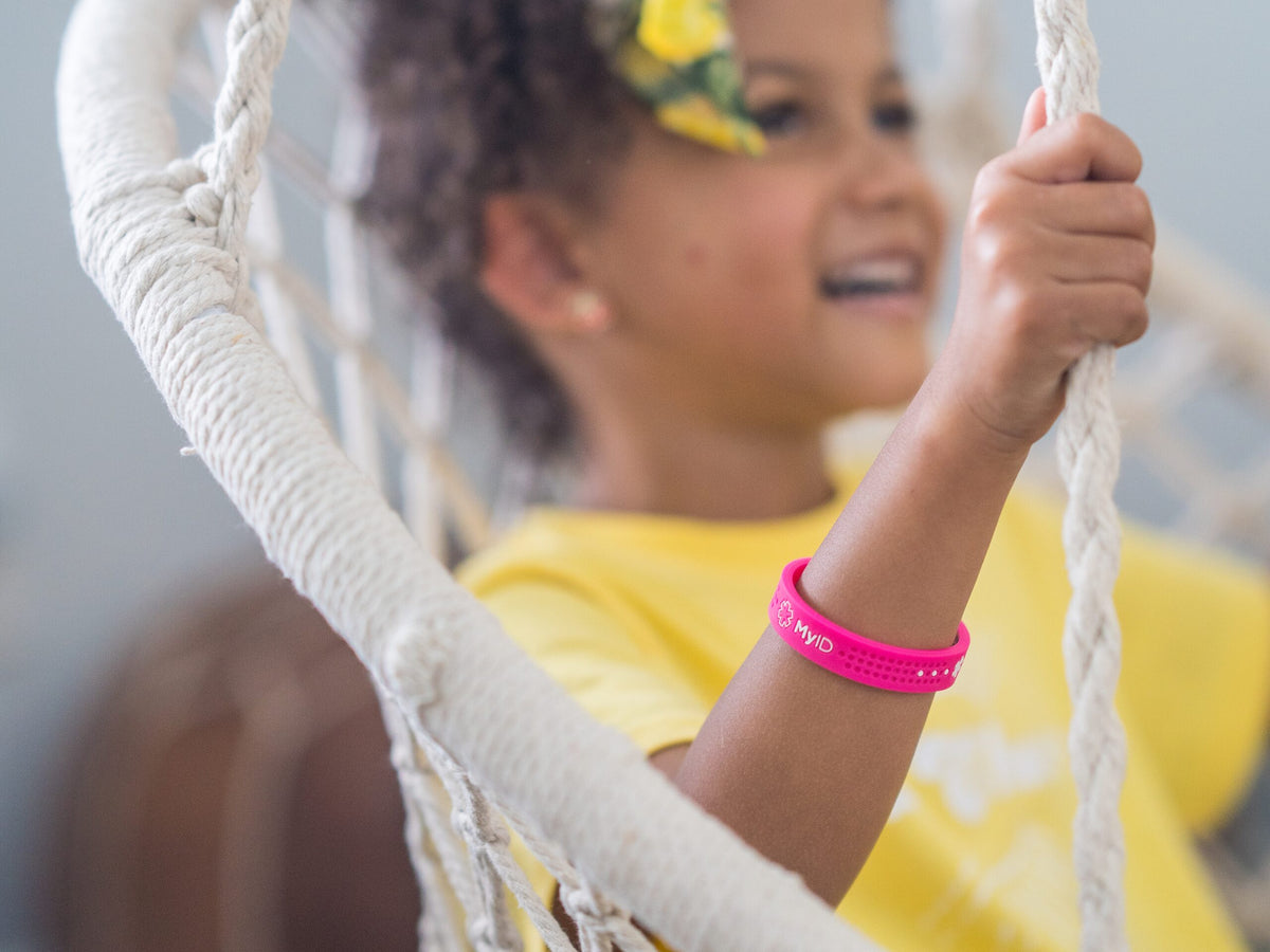 Smiling girl on a swing wearing a pink MyID Sport medical ID bracelet